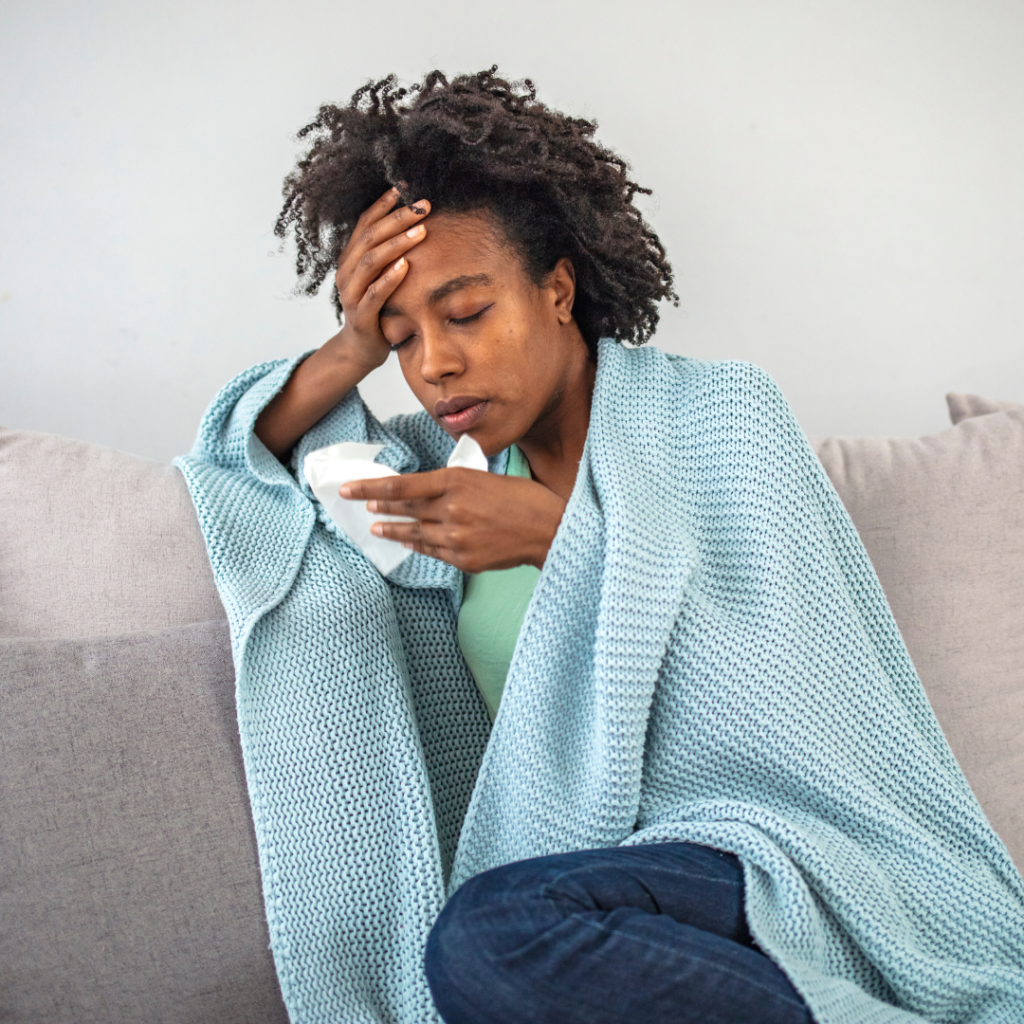 A sick woman sitting on her couch wrapped in a blanket 